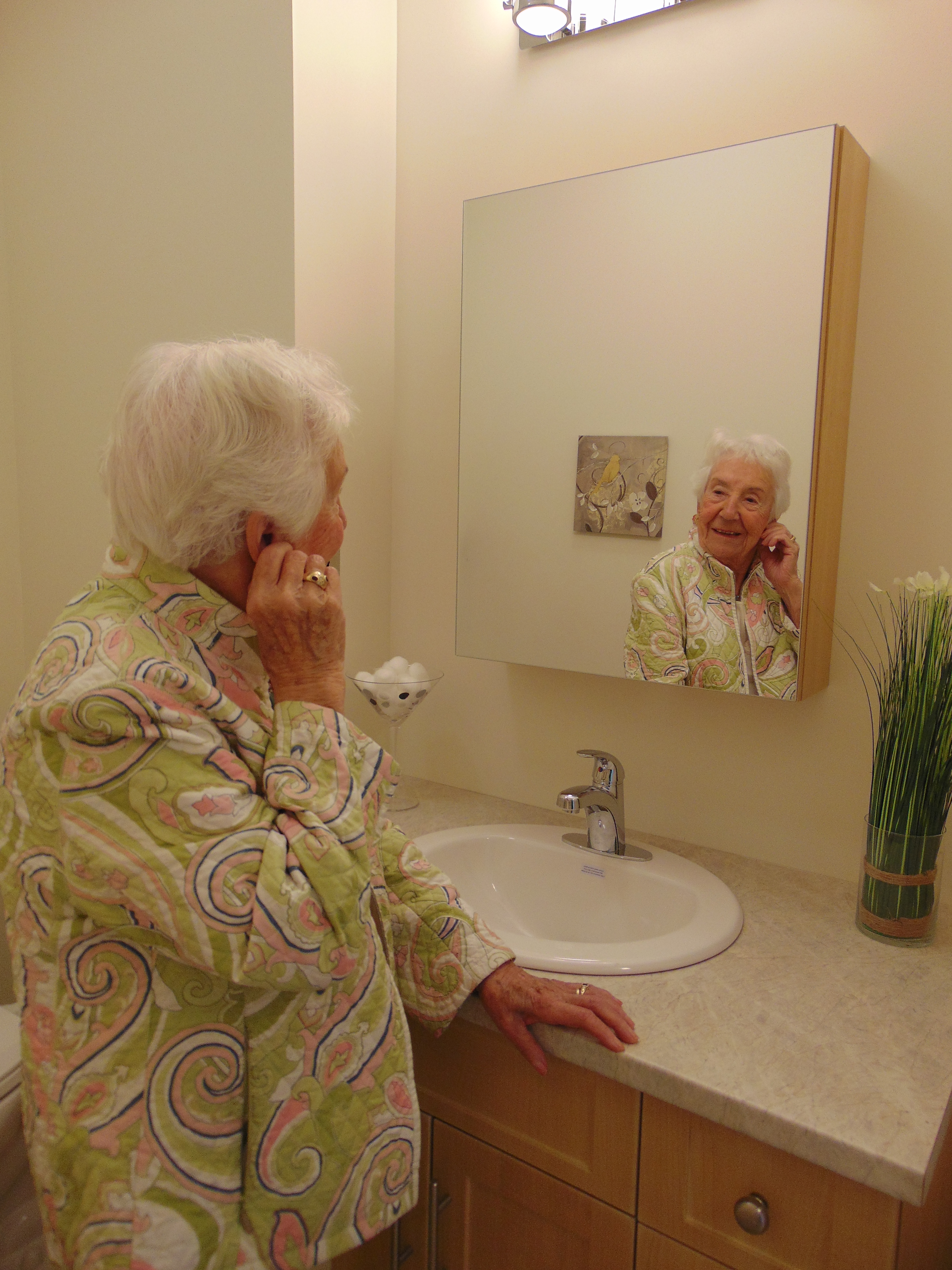 Senior Lady putting earrings on in powder room mirror